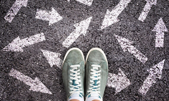 Turnschuhe und Pfeile, die in verschiedene Richtungen auf Asphaltboden zeigen