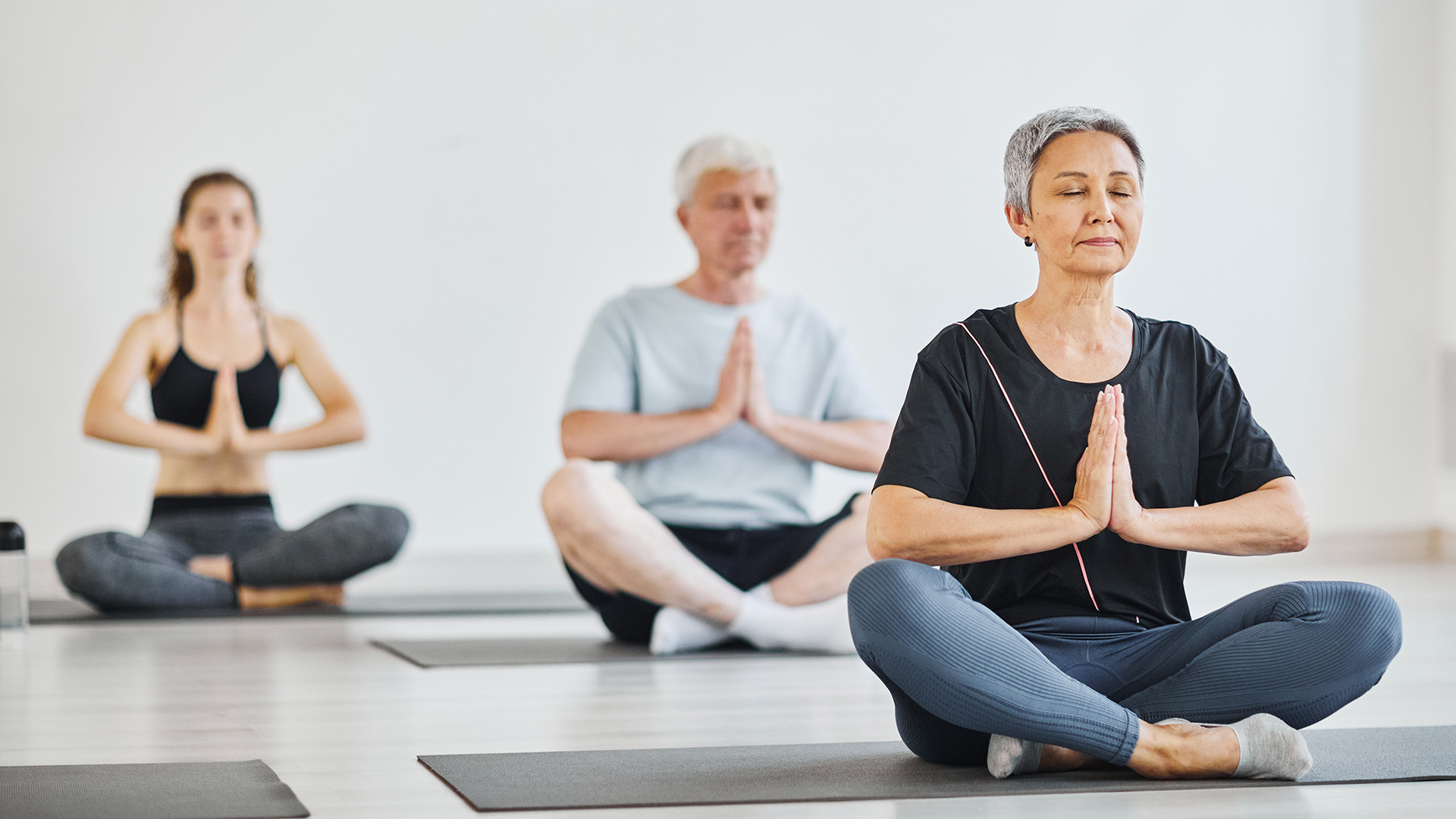 Menschen sitzen auf Matten im Lotussitz mit geschlossenen Augen und meditieren während einer Yoga-Stunde