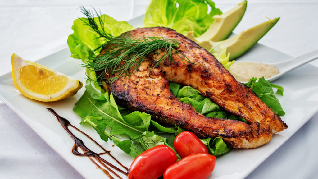 Frisch gebratener Fisch auf Salatbett mit Garnierung auf einem Teller
